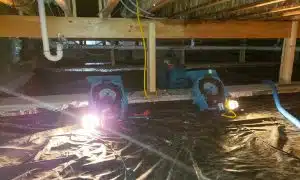 a water-damaged crawl space under repair with equipment and lights