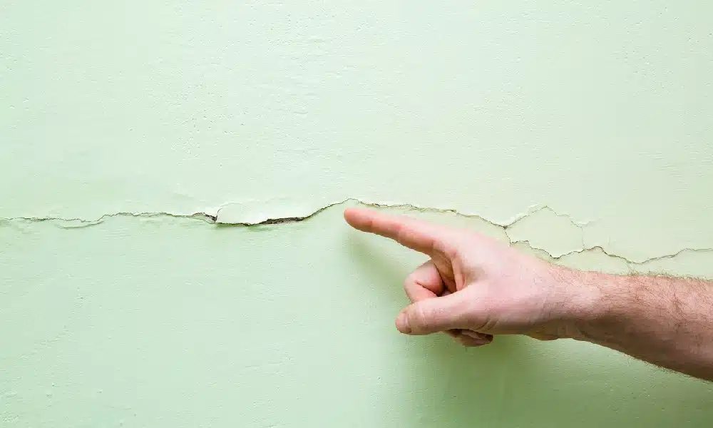 A man’s finger points to a horizontal crack in a wall