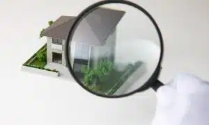 a model of a home under a magnifying glass, symbolizing a home foundation inspection