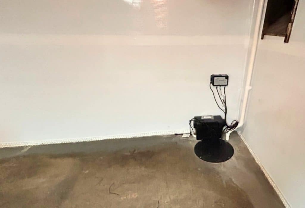 Installed interior basement waterproofing with vapor barrier, edge drain, sump pit with lid and white discharge pipe in Fairfax, VA.