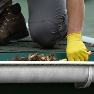 A man cleaning clogged gutters to prevent water overflow and potential damp basement in Manassas, VA