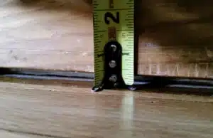 A gap with measuring tool, illustrating gaps between floor and baseboard as sign of unlevel basement slab floor in Bristow, VA.