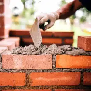 A person applying a cement mixture to the foundation bricks, showing improper construction or substrate may cause mortar cracks in Flint Hill, VA