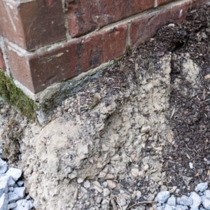 An image showing an outside damaged foundation of a house, highlighting how improper slope can be a cause of a damp basement