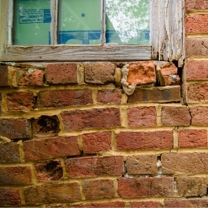 A damaged brick foundation wall near a window, showing poor maintenance as a cause of sticking doors and windows in Clear Brook, VA.