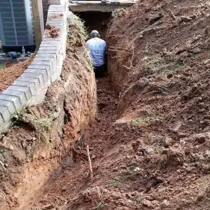 A man digging soil near a foundation to address damp basement in Ashburn, VA, shows how soil type can contribute to the problem.