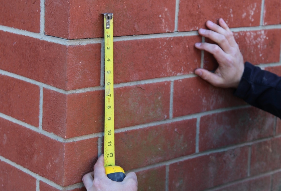 A foundation inspector measuring the exterior foundation crack.