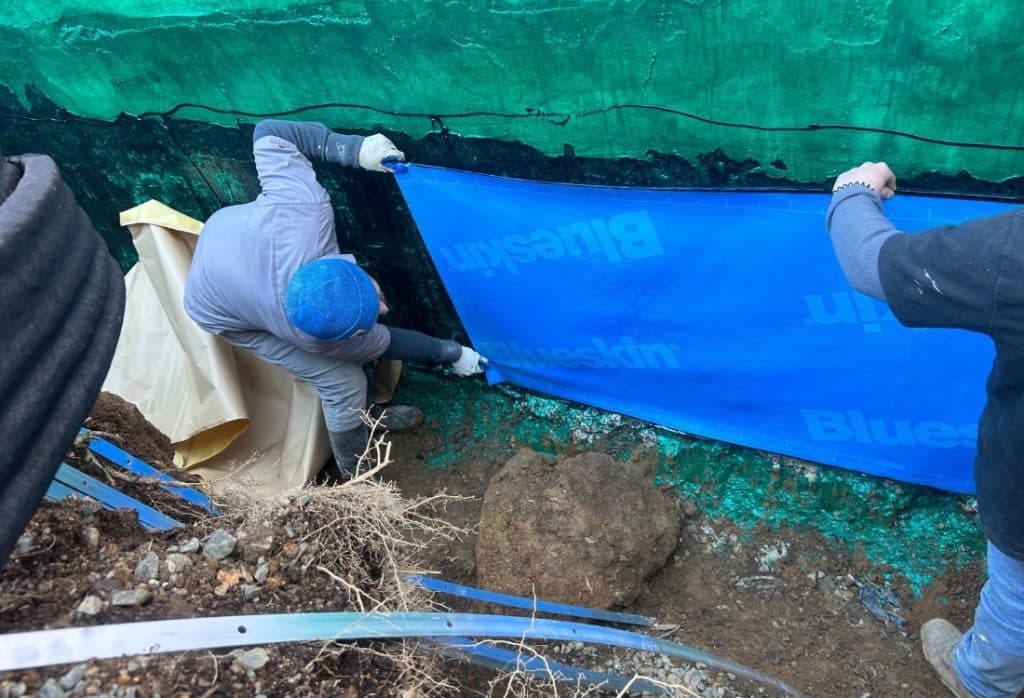Waterproofing contractors applying waterproof membranes to the exterior foundation walls.