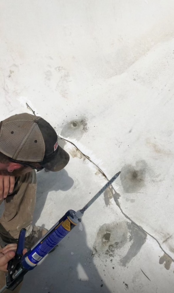A concrete caulking contractor applies Polyflex sealant to repair cracks in a sidewalk, ensuring long-lasting protection.