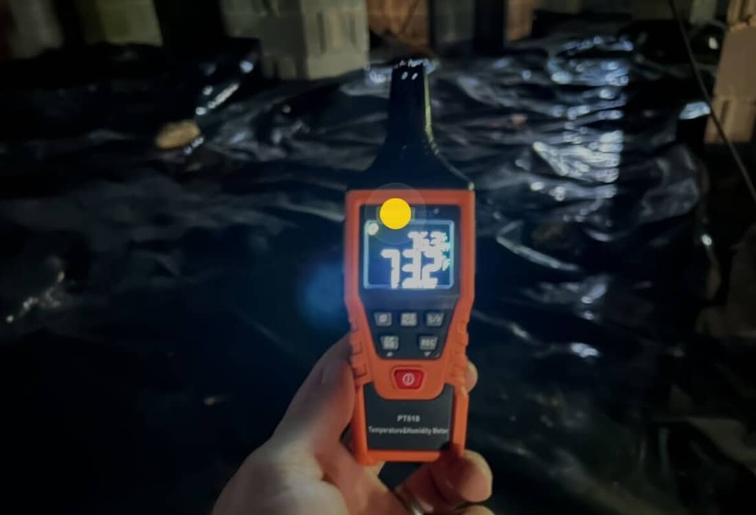 Hygrometer measuring reduced humidity level in crawl space after dehumidifier installation.