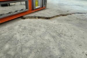A tool measuring large cracks in a basement floor near the wall, showing signs of an uneven basement floor in Alexandria, VA.