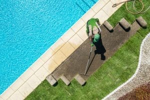 Man removing grass around the pool deck with water seepage, highlighting poor drainage as a sign of a sunken deck in Ashburn, VA.