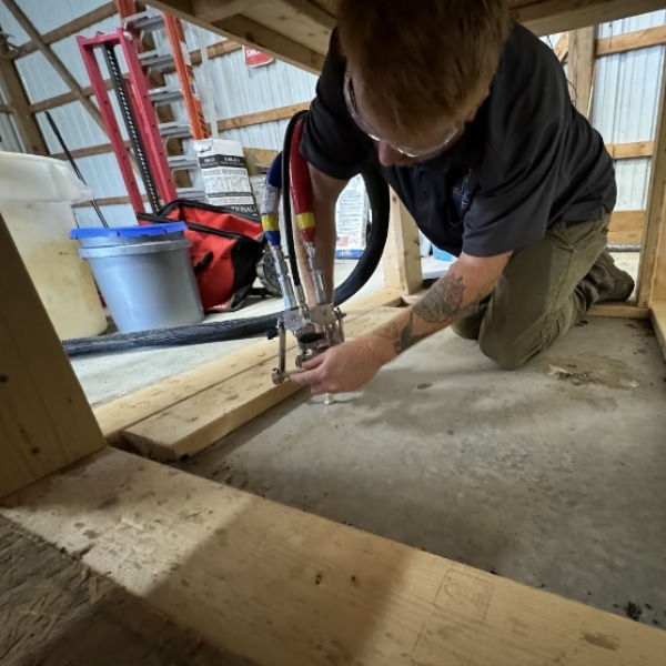 A technician injecting polyurethane foam beneath a sunken concrete slab to lift it caused by soil settlement in Martinsburg, WV.
