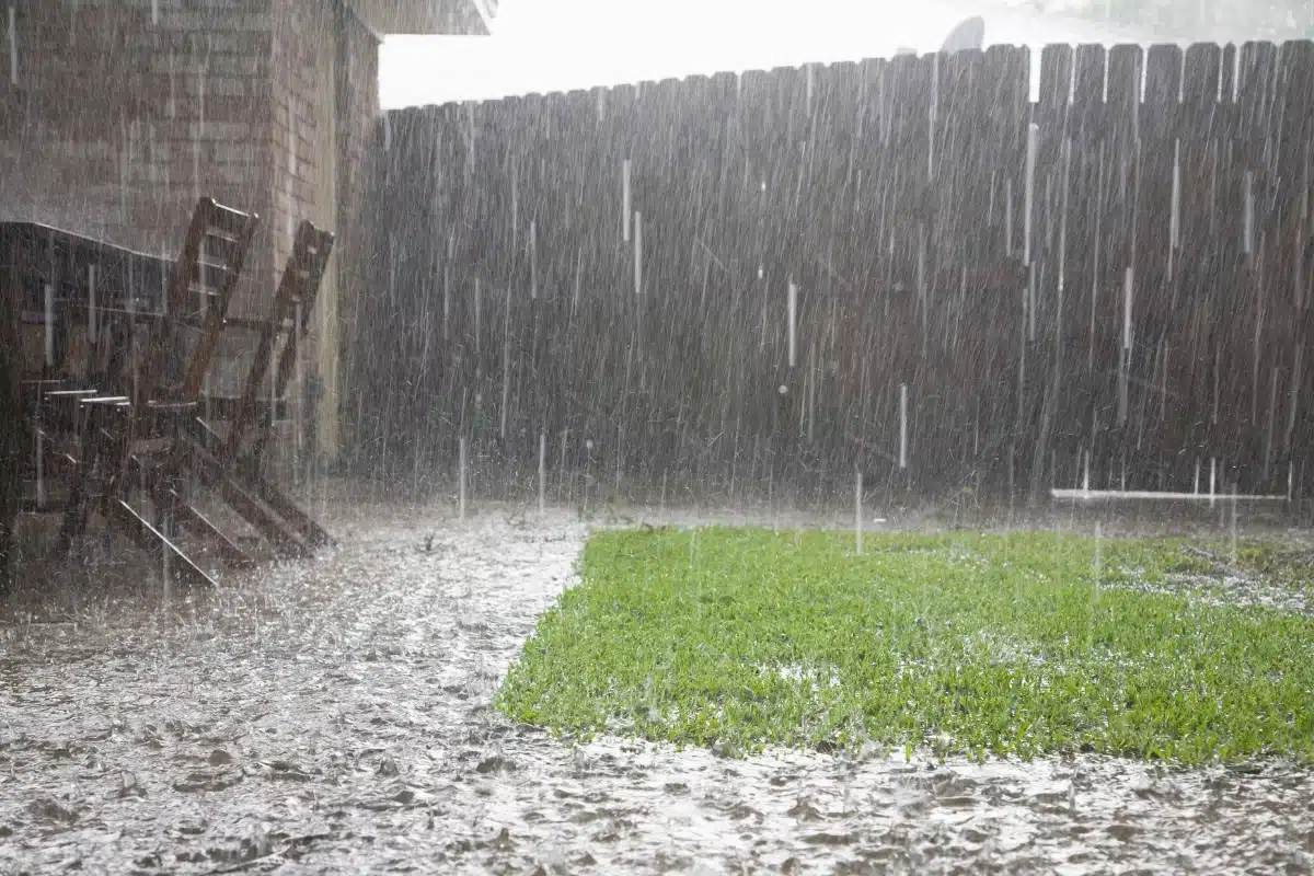 Heavy rain saturating sloped terrain near a home, contributing to basement water seepage and slope failure in Gainesville, VA.