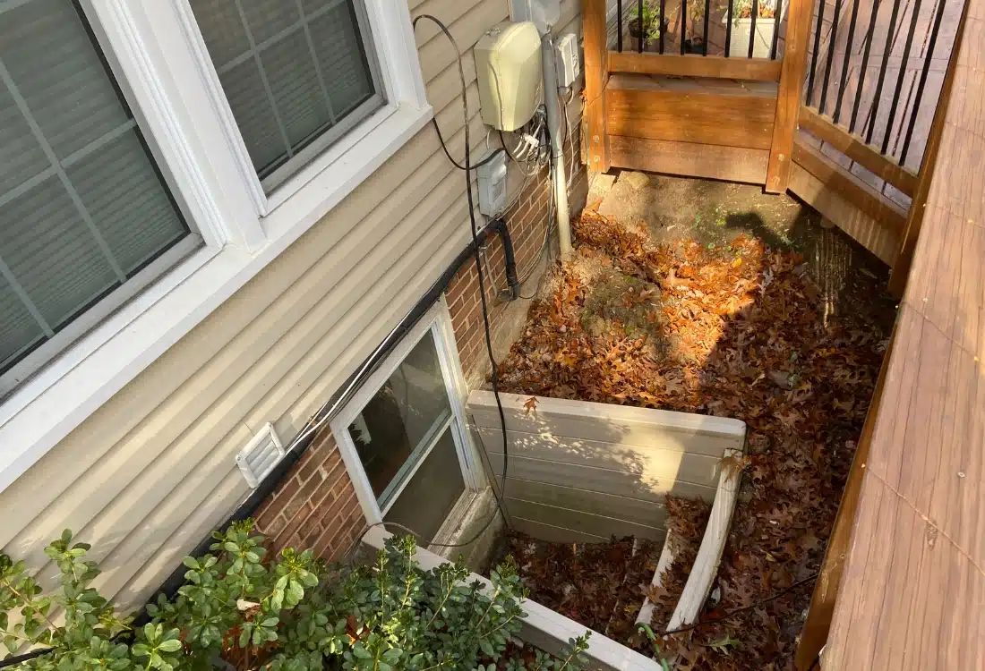 Outdated window well with rainwater stains in the foundation wall that needs drainage solutions in Alexandria, VA.