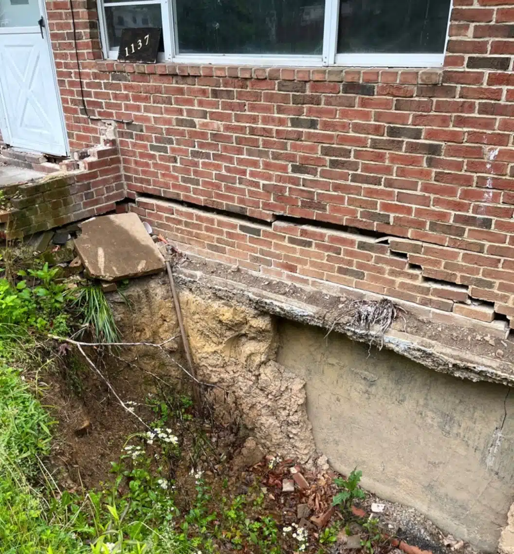 Close-up of a cracked home foundation with uneven settling, needing soil compaction solutions in Fairfax, VA.