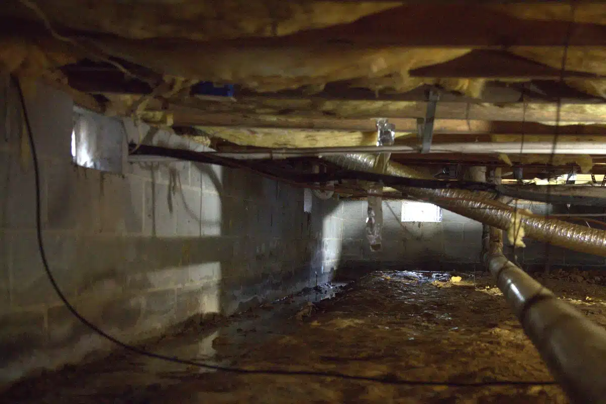 Unsealed muddy dirt crawl space affected by seasonal temperature changes caused by open crawl space vents in Ashburn, VA.