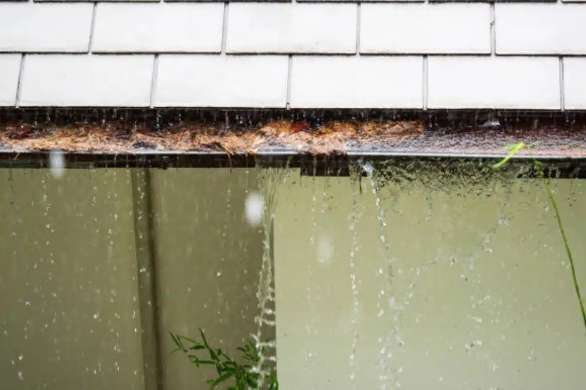 Clogged gutter overflowing during heavy rain in Ashburn, VA, causing water pooling near the foundation and crawl space issues.