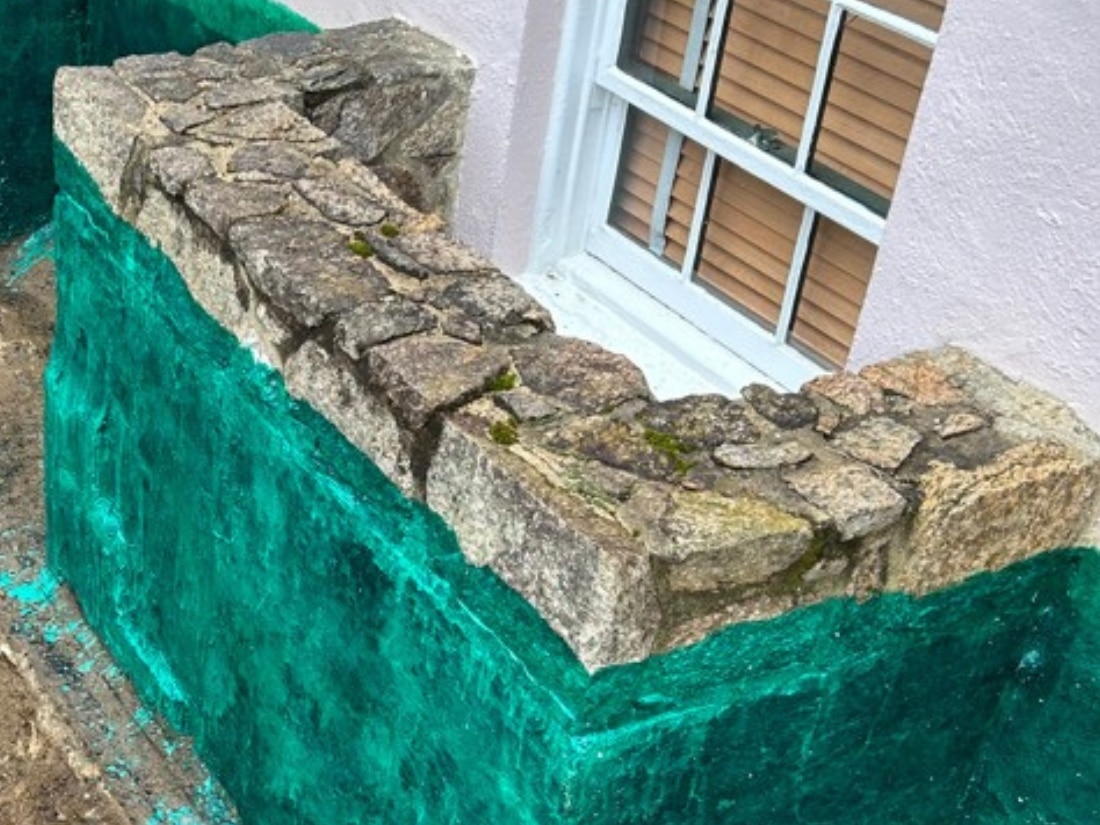 Masonry repair and parging applied to a deteriorated stone window well as part of exterior waterproofing in Fredericksburg, VA.