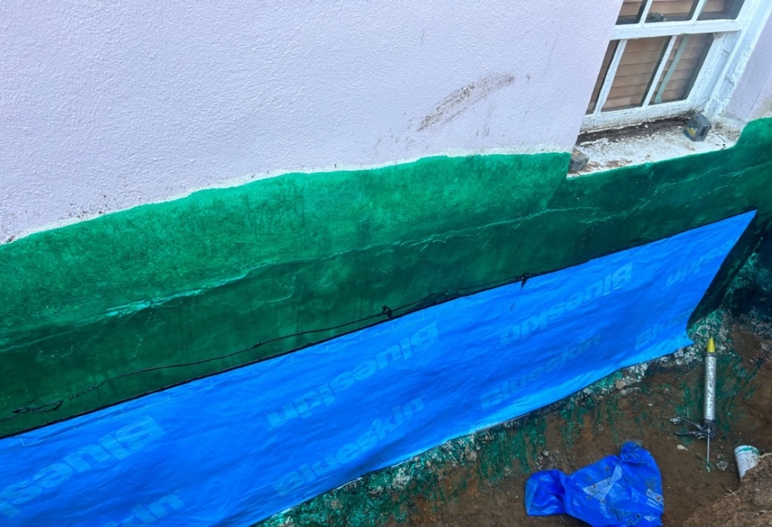 Waterproofed exterior foundation wall of a historic home in Winchester, VA, with reinforced stone window wells and drainage.