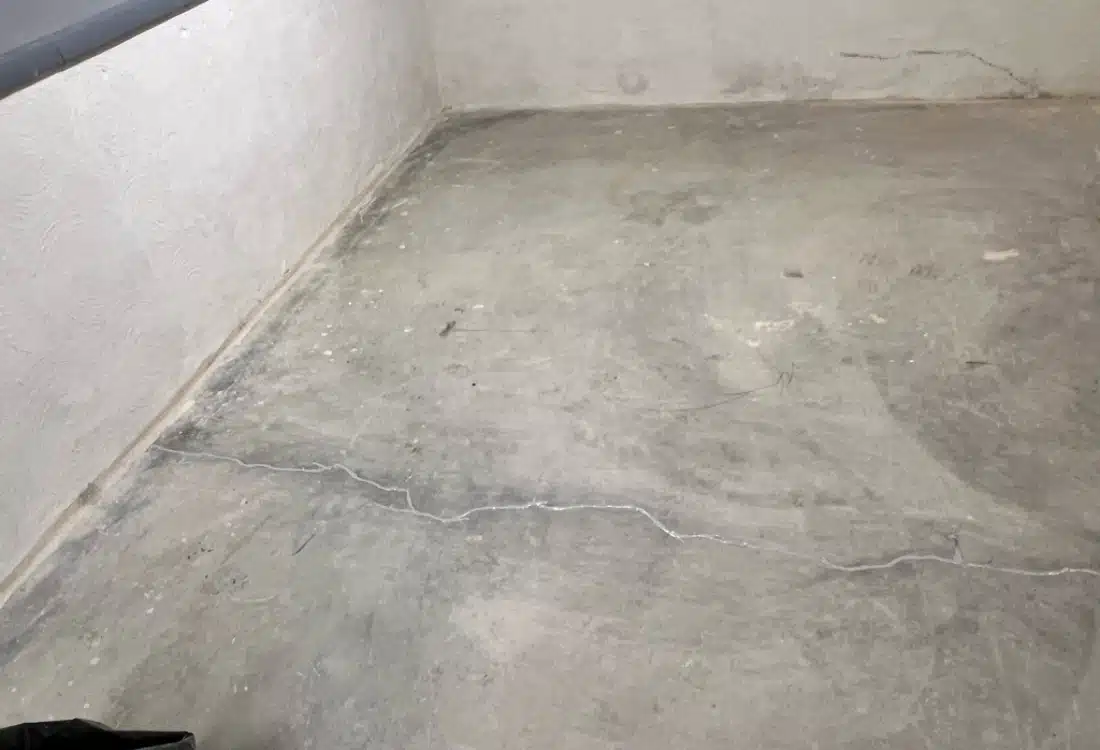 Basement floor with water seepage stains and cracks before the interior basement drainage system installation in White Post, VA.