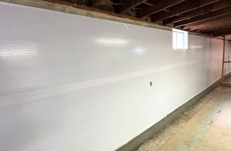 Basement wall with installed vapor barrier and drainage system, illustrating interior basement waterproofing in Alexandria, VA.