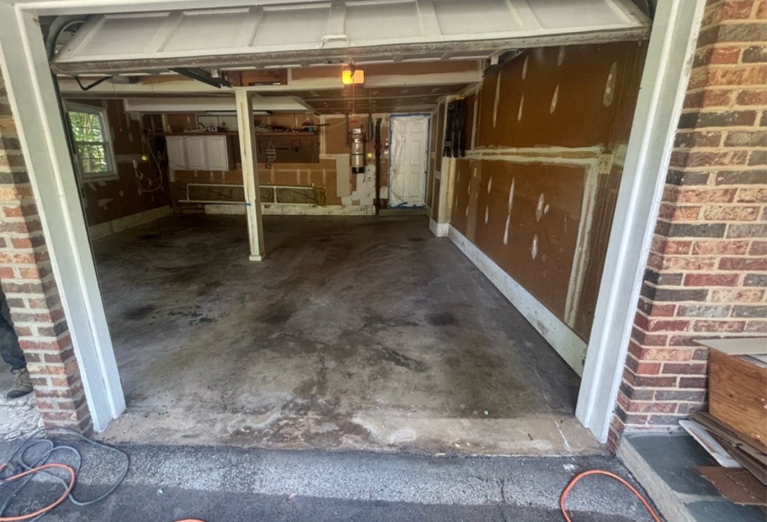 Damaged and sinking garage floor before repair in Fairfax, VA, with visible cracking and water pooling near the entrance.