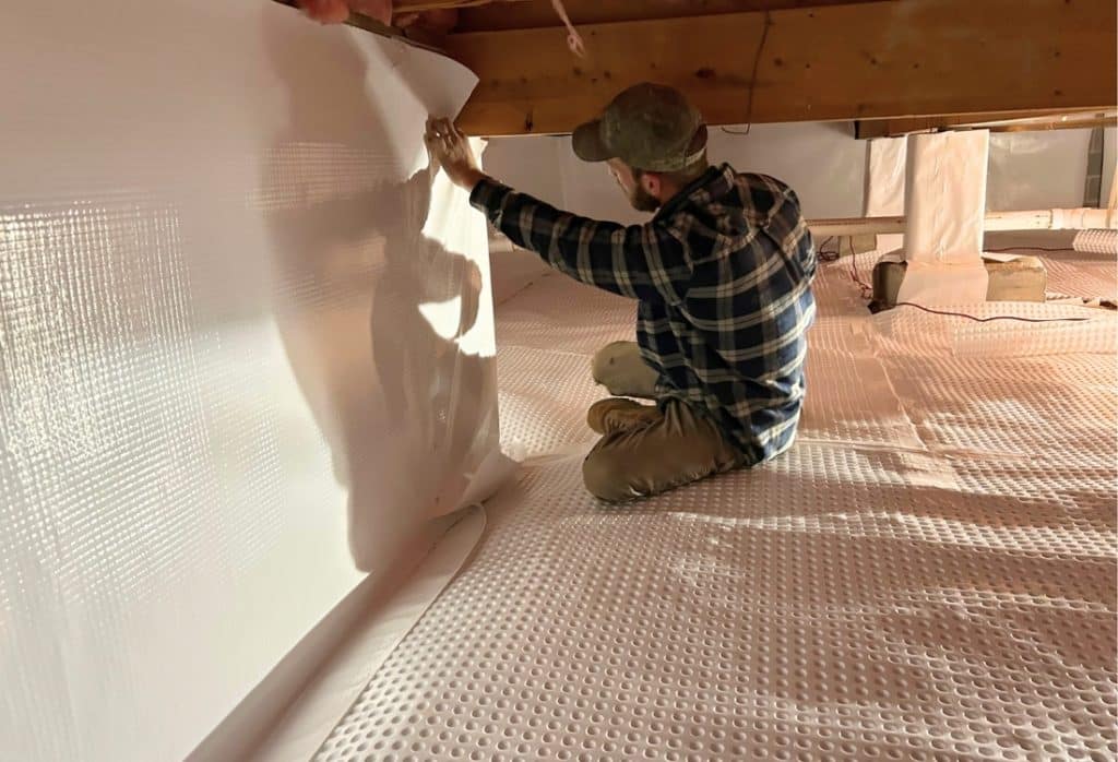 An expert sealing crawl space with a vapor barrier and insulation, a process of crawl space encapsulation in Alexandria, VA.