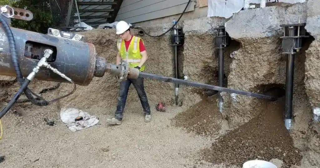 Worker installing helical tieback anchors to stabilize and reinforce a bowing foundation wall in Berryville, VA.