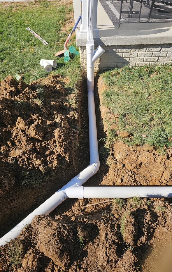 Connected buried downspout extensions installation in Fairfax, VA, to improve rainwater drainage and protect a home foundation.