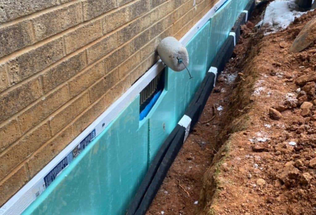 Exterior basement waterproofing method in Harpers Ferry, WV, showing membrane and insulation installed to prevent moisture seepage.