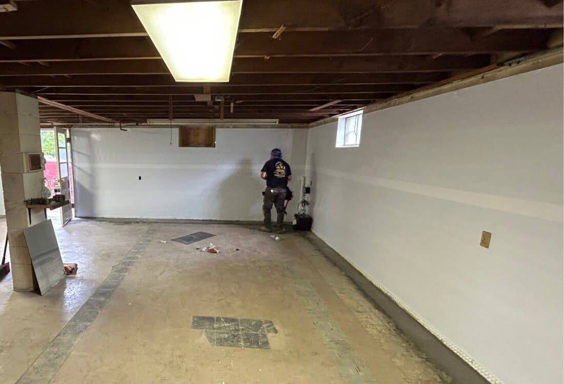 An expert installing an interior basement waterproofing system with drainage and a vapor barrier for water control in Alexandria, VA.