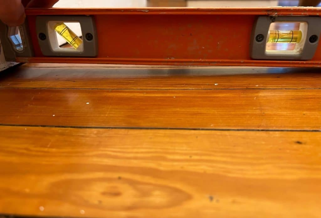 A carpenter’s level placed on a wood floor shows the surface is not level, a visible sign of cracked joists in White Post, VA.