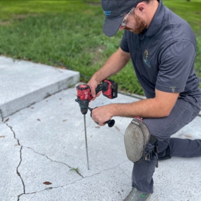 Technician sealing long cracks in an exterior concrete slab to protect and stabilize a sinking concrete slab in Manassas, VA.