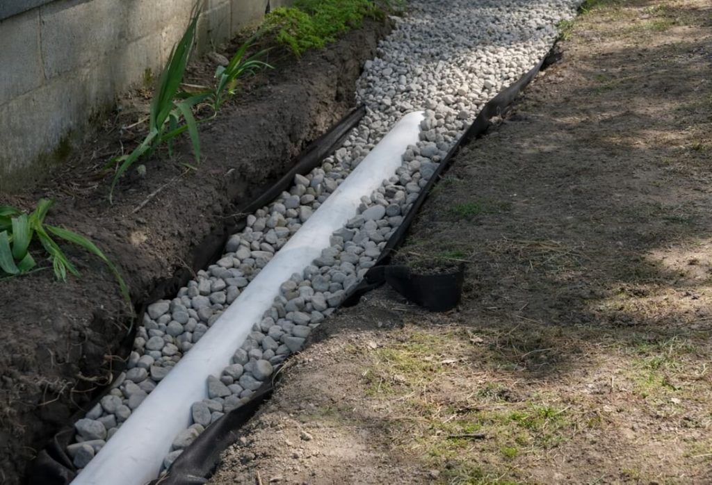 Installed exterior French drain in Winchester, VA, with perforated pipe surrounded by gravel in a trench, redirecting groundwater away.