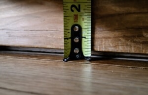 Measuring tape showing gap between hardwood floor and baseboard trim, a sign of uneven basement floor in Bristow, VA.