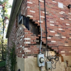 Brick foundation wall with visible stair-step cracking and settlement damage, causing uneven basement floor in Brambleton, VA.