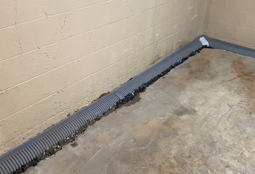 Installed interior French drain in Winchester, VA, with perforated pipe in basement floor wall joint to collect and redirect groundwater.