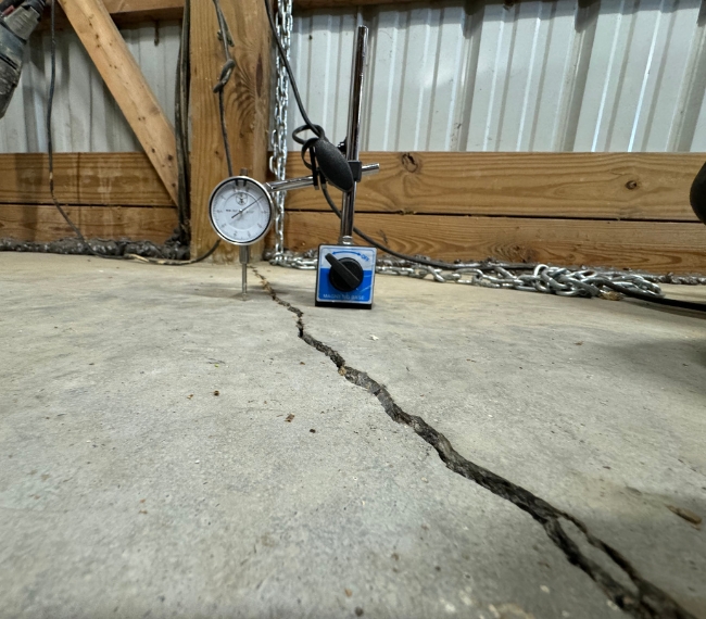Cracked, sinking basement concrete slab with floor settlement gauge, needing sinking concrete slab repair in Winchester, VA.