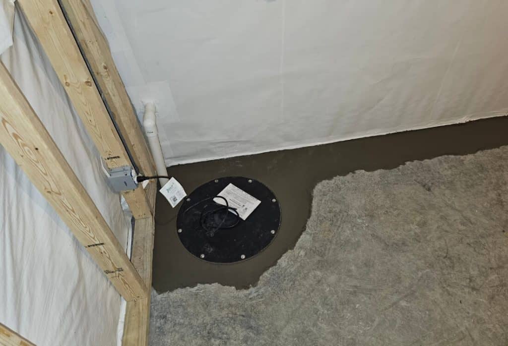 Installed sump pump basin in Winchester, VA, basement floor with sealed cover and discharge pipe to remove collected groundwater.