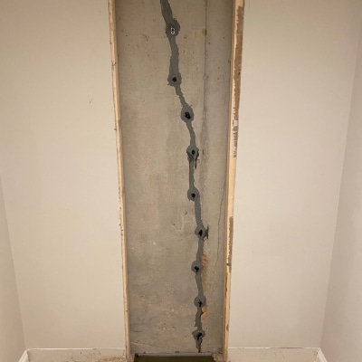 Close-up of a basement wall crack being sealed with polyurethane injection to stop active water seepage through the foundation wall.