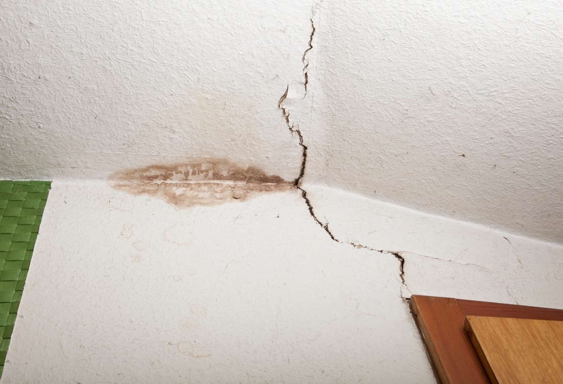 Ceiling crack with water staining and discoloration at the wall junction, a sign of moisture damage requiring expert evaluation