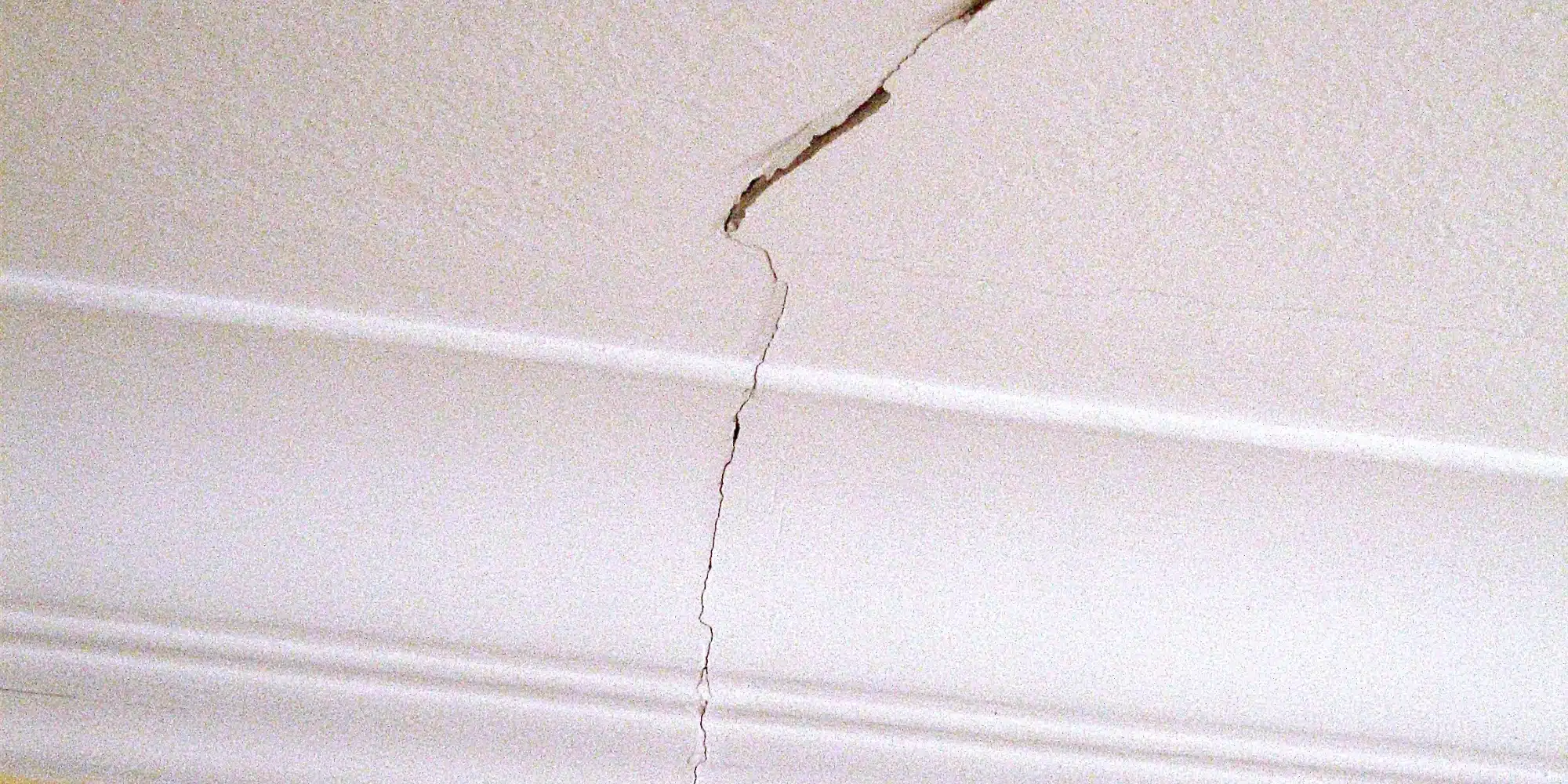 Ceiling crack running through crown molding down the wall that may indicate foundation or structural issues