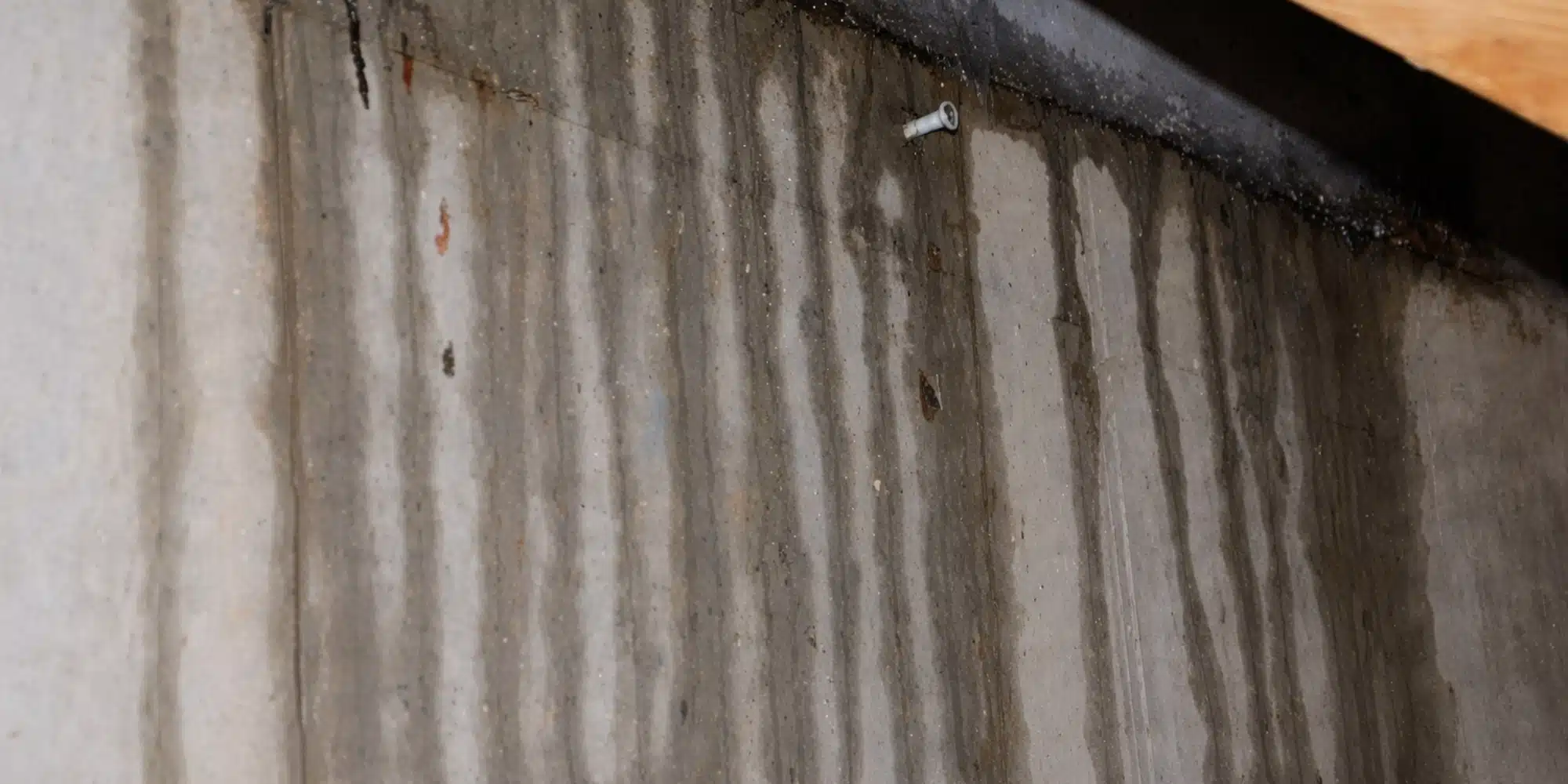 Water seeping through a cracked basement wall, leaving wet stains and mineral deposits on the concrete surface below the crack.
