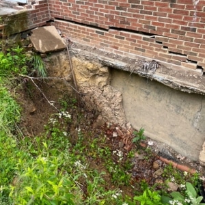 Exposed foundation footing with visible soil erosion and undermining beneath, causing bowing foundation wall in Harpers Ferry, WV.