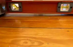 A level tool on a hardwood floor showing an unlevel surface indicating signs of bowing foundation wall in Charles Town, WV.