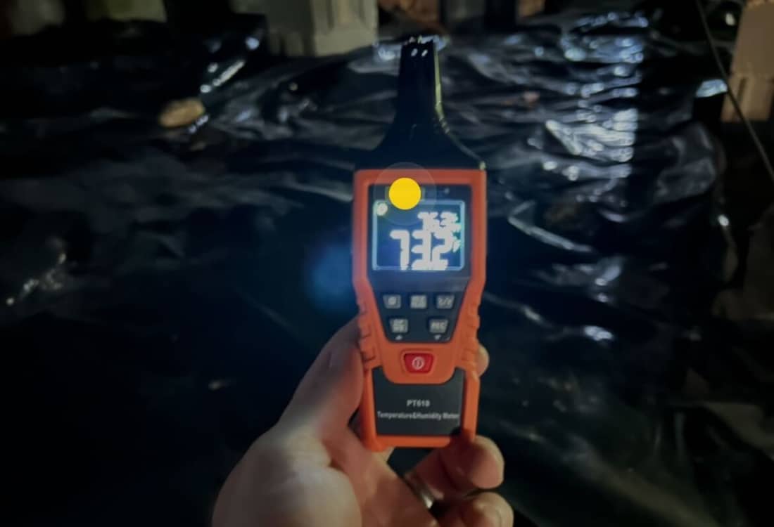 A hygrometer held inside a dark crawl space reads 73 percent humidity, factors causing crawl space mold in Fairfax, VA.