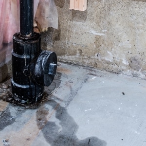 Leaking basement pipe with water pooling on concrete floor causing moisture damage and water stains in Berryville, VA.