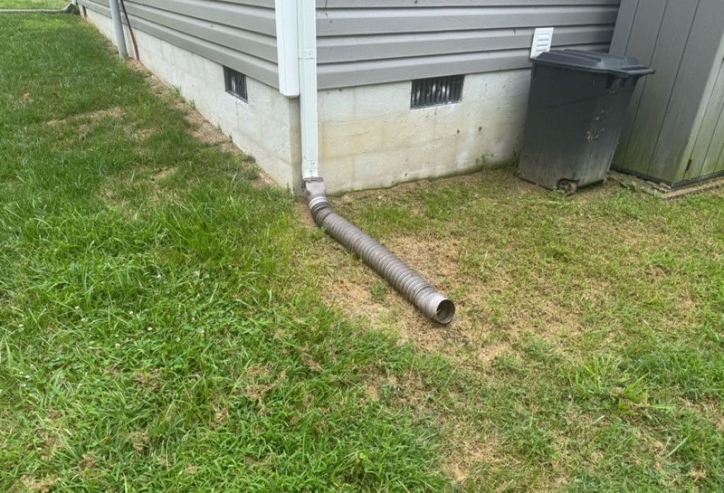 Corrugated flex downspout on grade discharging water directly at foundation base before replacement in Shenandoah, VA.