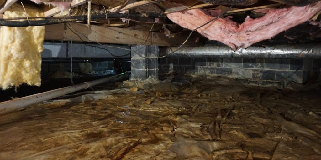 Dark and damp crawl space with exposed floor joists and bare dirt floor, a condition causing bad crawl space odor in Northern, VA.